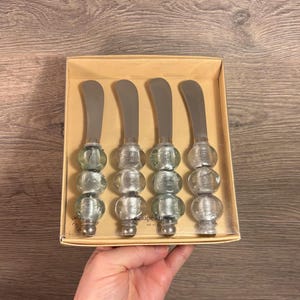 May include: Set of four silver and blue glass beaded butter knives in a clear plastic package. The package has a brown cardboard backing with the text "Canape Knives Set of 4".