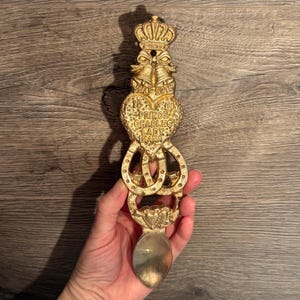 Könnte beinhalten: Ein goldfarbener Gedenklöffel mit Krone, Glocken und einem herzförmigen Design. Der Löffel ist mit "29. Juli 1981" und "Prince Charles Lady Diana" graviert.