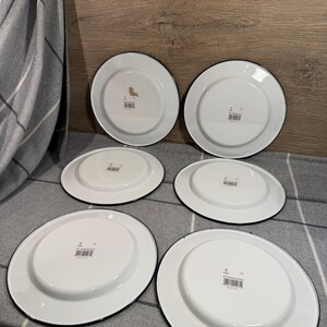 Pode incluir: Um conjunto de seis pratos de esmalte branco com bordas pretas, dispostos em duas filas. Cada prato apresenta uma base circular central, uma borda plana e uma pequena etiqueta retangular com c&oacute;digo de barras na parte inferior.