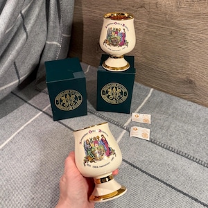 Puede incluir: Copa de cerámica color crema con ribete dorado, con un escudo colorido y texto que conmemora el 150 aniversario de la Orden Independiente de Rechabitas. La copa se muestra con su caja original.