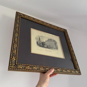 May include: Framed black and white architectural print of Somerset House, London, with a gold ornate frame. The print is set against a dark gray matting. The frame has a detailed, carved design.