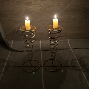 Peut inclure: Deux bougeoirs en m&eacute;tal dor&eacute; avec un design en spirale. Chaque bougeoir a une bougie blanche sur le dessus.