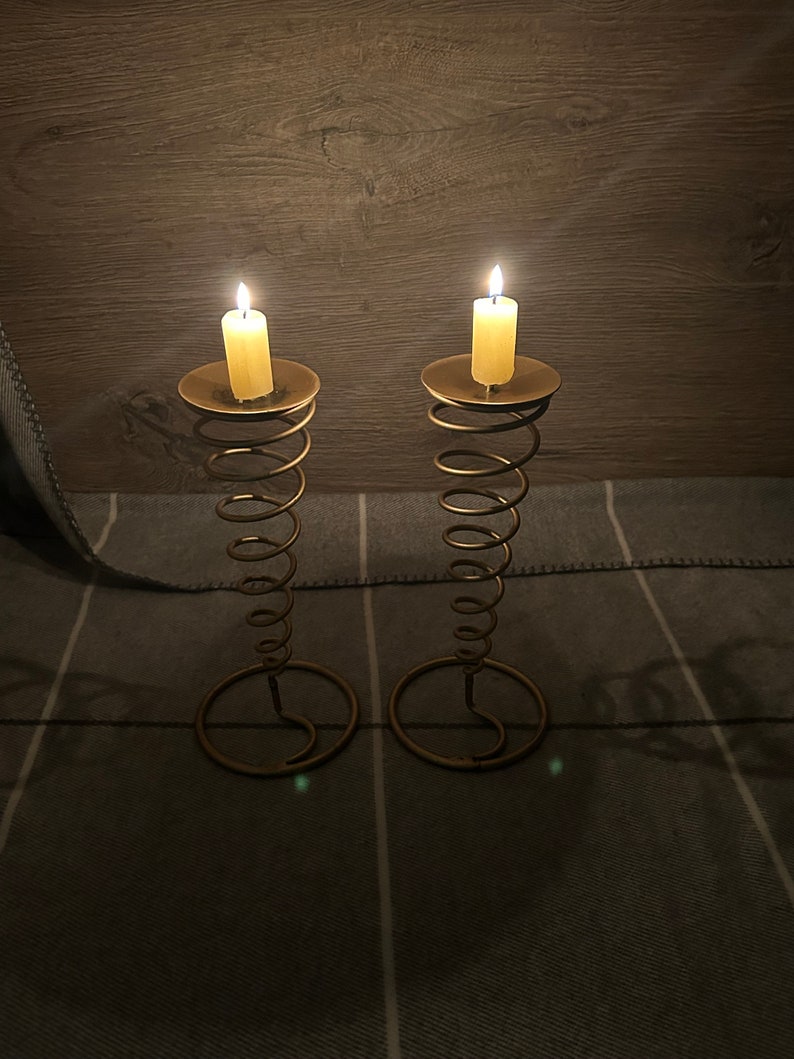 Peut inclure: Deux bougeoirs en m&eacute;tal dor&eacute; avec un design en spirale. Chaque bougeoir a une bougie blanche sur le dessus.