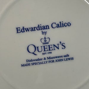 May include: A white ceramic saucer with blue text that reads "Edwardian Calico by QUEEN'S EST 1795 Dishwasher & Microwave safe MADE SPECIALLY FOR JOHN LEWIS".
