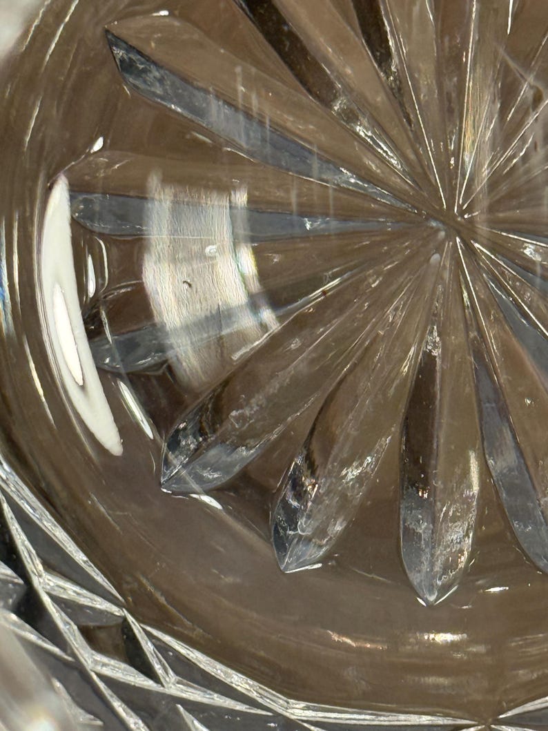 Op de afbeelding: Close-up van een helder glazen object met een stervormig patroon aan de basis. Het glas heeft een facetontwerp rond de rand. De afbeelding benadrukt de helderheid en ingewikkelde details van het glaswerk.