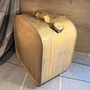 May include: A vintage, cream-colored metal container with a handle and a cap. The container has a rectangular shape with rounded edges and a distressed finish, suggesting age and use. The overall aesthetic is rustic and industrial.