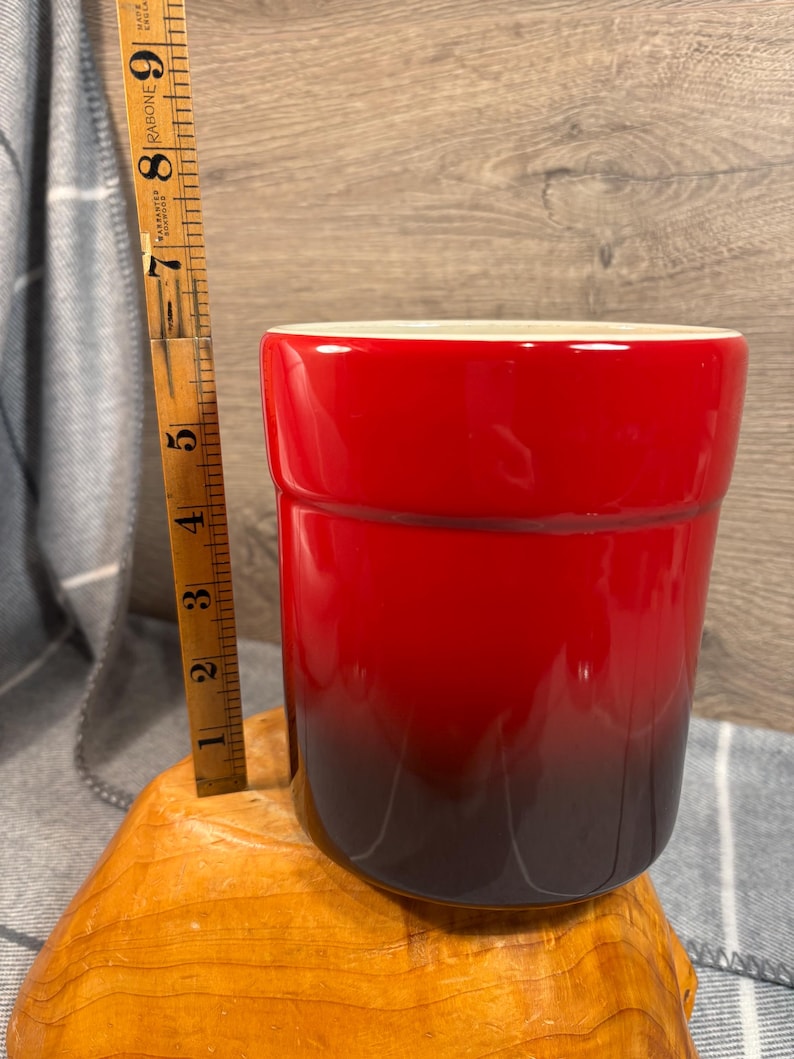 May include: A red and black ceramic utensil holder. The holder is cylindrical and has a gradient color scheme, transitioning from red to black.