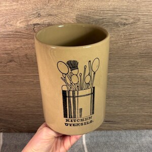 Puede incluir: Un porta utensilios de cerámica de color beige con una ilustración en blanco y negro de utensilios de cocina y el texto "KITCHEN UTENSILS."
