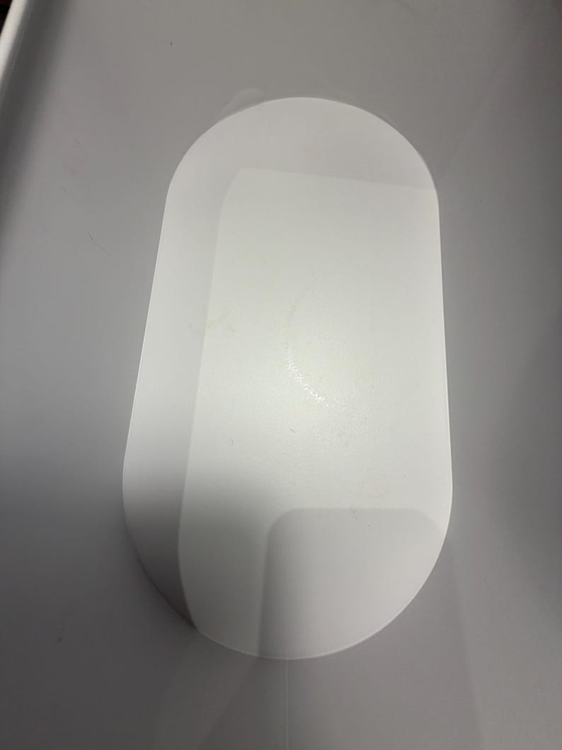 May include: A solid white, oval-shaped tray with a smooth, matte finish and rounded edges. The tray features a flat, elongated surface with a slightly raised rim, providing a clean and simple design for holding small items on a flat surface.