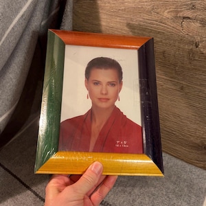 Peut inclure: Un cadre photo rectangulaire avec un cadre en bois multicolore. Le cadre a une bordure verte, orange, jaune et bleu marine. Le cadre contient un portrait de femme. Les dimensions du cadre sont de 18 x 13 cm.