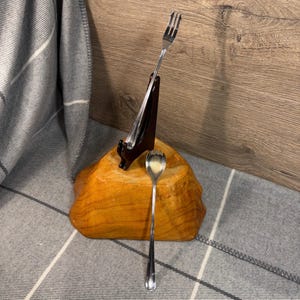 May include: A wooden stand with a brown base and a black holder for a fork. A silver fork and spoon are displayed on the stand.