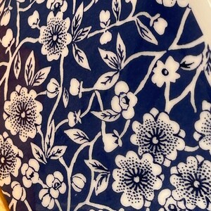 May include: A close-up of a blue and white ceramic mug with a floral pattern. The mug features a repeating design of white flowers and leaves on a dark blue background.