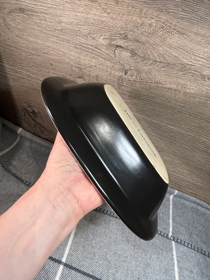 May include: A black, oblong-shaped serving dish with a white interior. The dish has a glossy finish and a slightly curved design. The text "STONE & SULLIVAN" is visible on the interior.