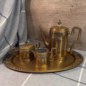 May include: A vintage brass tea set, comprising a teapot, creamer jug, sugar bowl, and serving tray. The set has intricate detailing and a warm, golden colour. The teapot features a tall spout and a decorative handle.