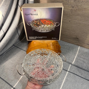 May include: Silver-plated serving dish with a clear glass insert divided into three sections. The dish has a decorative border and is labeled "Royal Warwick Quality Giftware" on the box.