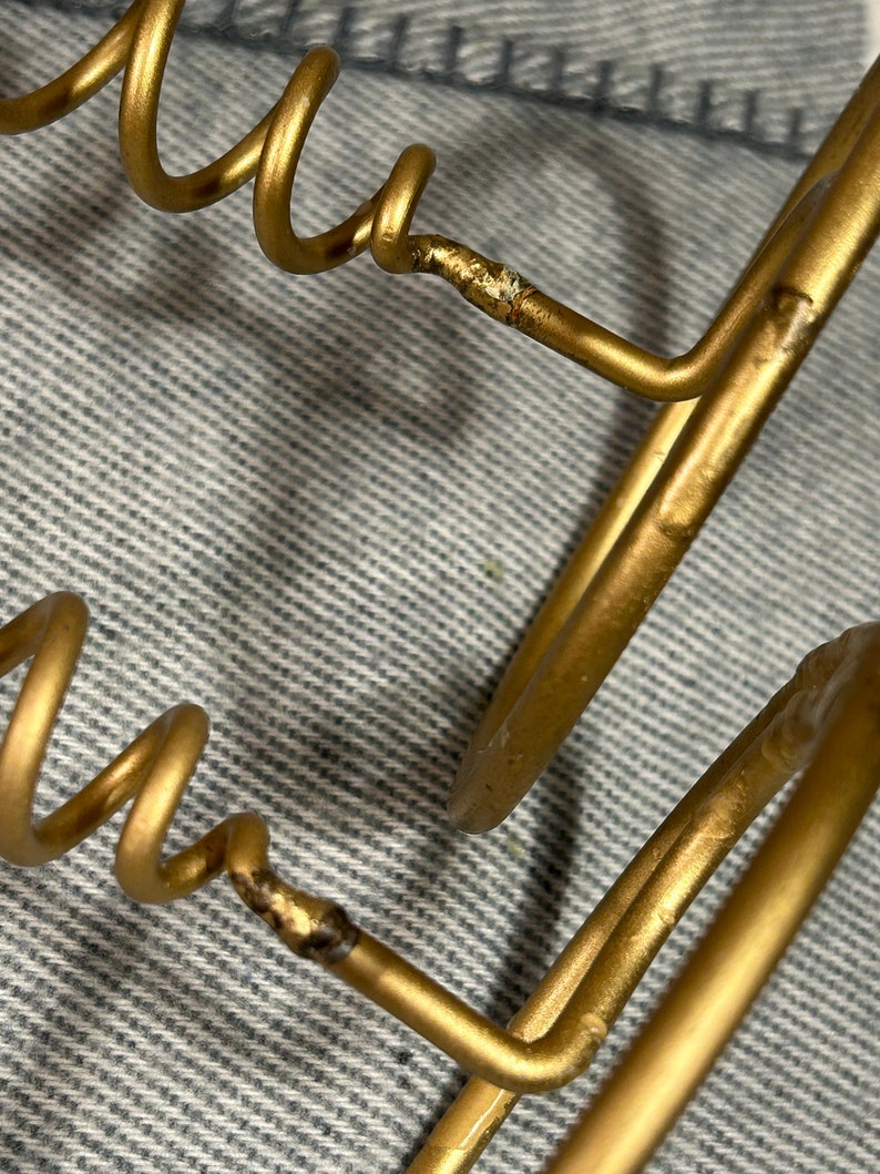 Peut inclure: Un porte-revues en fil m&eacute;tallique dor&eacute; avec un design en spirale. Le porte-revues est compos&eacute; de deux fils m&eacute;talliques qui sont pli&eacute;s en forme circulaire puis assembl&eacute;s. Le fil est lisse et brillant.