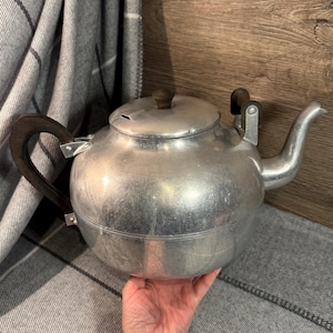 May include: A silver aluminium teapot with wooden handles. The teapot has a rounded body and a spout on the side.