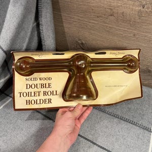May include: A solid wood double toilet roll holder in a package. The holder is a dark brown color and has a classic design. The packaging includes the text "Solid Wood Double Toilet Roll Holder".
