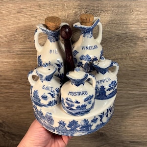 May include: Blue and white porcelain condiment set with a wooden stand. The set includes bottles for oil, vinegar, salt, pepper, and mustard.
