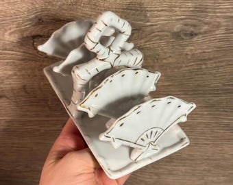 May include: A white ceramic decorative piece featuring a rectangular base with three fan-shaped elements and a bamboo-like structure. The fans and bamboo have gold accents. The piece is likely a decorative item for a home.