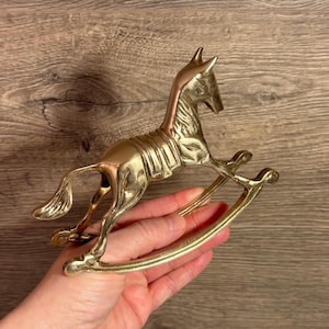 May include: A gold-coloured rocking horse figurine. The horse is detailed with a saddle and bridle. The rocking base is made of metal.