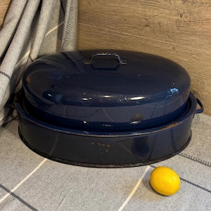 Könnte beinhalten: Eine dunkelblaue ovale Emaille-Bratform mit Deckel. Die Bratform hat ein leicht abgenutztes Aussehen mit einigen Rostflecken auf der Oberfläche.
