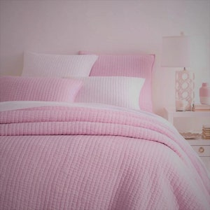 May include: A pink quilted bedspread with white and pink pillows. The bedspread has a subtle texture and is made of a soft, comfortable fabric.
