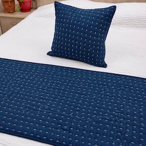 May include: A square throw pillow and a rectangular bed runner in deep navy blue fabric. Both items feature a quilted texture with a repeating pattern of small, horizontal white stitched lines across the entire surface of the dark blue textile.