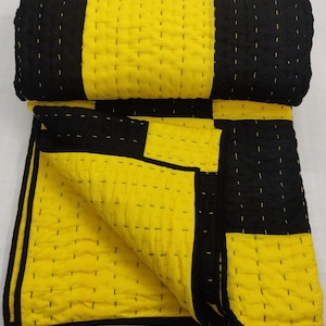 May include: A folded, quilted blanket with a bold checkerboard pattern in black and yellow. The blanket is made of a soft, textured fabric and features visible stitching throughout. The edges are neatly finished with a black border.