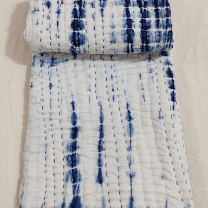 May include: White and indigo blue tie-dye patterned quilt. The quilt is folded and rolled, revealing the indigo blue pattern. The quilt is made of a soft material and has a stitched design. The quilt is a decorative home textile.