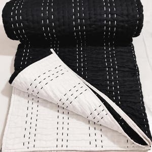 May include: A reversible quilted blanket featuring a black side with white vertical running stitch patterns and a white side with black vertical running stitch patterns. The fabric has a textured, crinkled appearance throughout the entire surface.