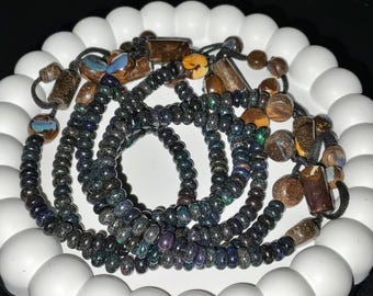 May include: Several beaded necklaces with a variety of natural stone beads in shades of brown, black, and iridescent colors. The necklaces are arranged on a white, scalloped-edge plate.