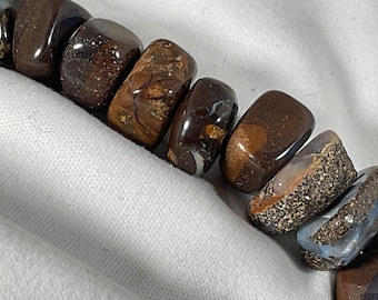 May include: A strand of brown, black, and blue opal beads. The beads are smooth and polished, and they have a variety of patterns and textures.