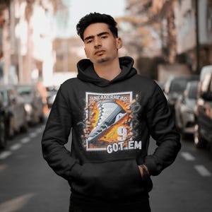 May include: Black hoodie with a graphic print of a white and grey sneaker breaking through a brick wall. The text "SNEAKERHEAD" and "GOT 'EM" are printed on the graphic.