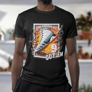 May include: Black t-shirt with a graphic of a white and grey sneaker breaking through a brick wall. The text "Sneakerhead 9 Got Em" is printed below the sneaker.
