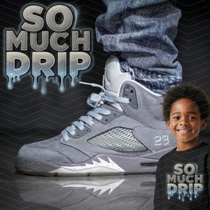 Può includere: Una sneaker alta grigia e bianca con il numero 23 sul lato. La scarpa è abbinata a jeans blu. Le parole "SO MUCH DRIP" sono visualizzate in un font a goccia. Un bambino indossa una maglietta nera con lo stesso testo.