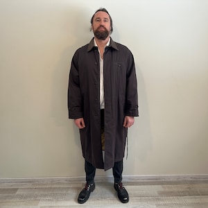 May include: A long brown coat with a collar and a belt. The coat is worn by a person with a beard and a white shirt.