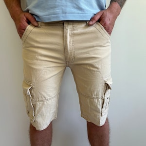 May include: Beige cargo shorts with two large pockets on the sides and two smaller pockets on the back.