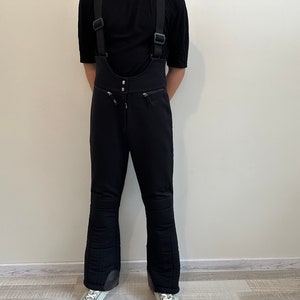 May include: Black ski trousers with braces. The trousers have a wide leg and are made of a thick, durable fabric.