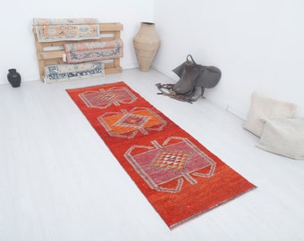 May include: A red, orange, and pink patterned runner rug with a geometric design. The rug is on a white floor.