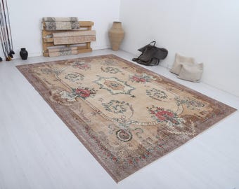 Puede incluir: Una alfombra rectangular grande con un diseño floral en tonos beige, marrón y rojo. La alfombra presenta un borde ornamentado y un medallón central. La alfombra está colocada sobre un suelo blanco.