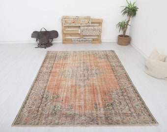 Pode incluir: Um tapete de estilo vintage com um fundo pêssego desbotado e uma borda com padrão marrom escuro e creme. O tapete tem um visual desgastado e é perfeito para adicionar um toque de estilo boêmio a qualquer cômodo.