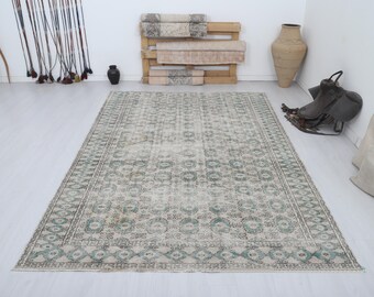 May include: A large, rectangular area rug with a distressed, vintage appearance. The rug features a muted color palette of cream, gray, and teal, with an intricate geometric pattern. The rug is placed on a light-colored wooden floor.
