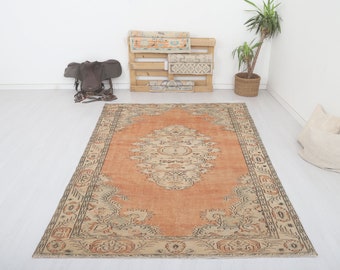 May include: A vintage-style rug with a peach-colored background and a beige floral pattern. The rug has a distressed look and a fringed edge.