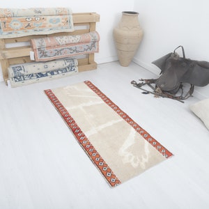 May include: A white runner rug with a red and blue geometric border. The rug is laid out on a white wooden floor.