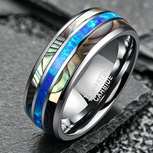 May include: A tungsten carbide ring featuring a central inlay of vibrant blue opal flanked by two strips of iridescent abalone shell. The interior of the band is polished silver-tone metal and is clearly engraved with the text TUNGSTEN CARBIDE.