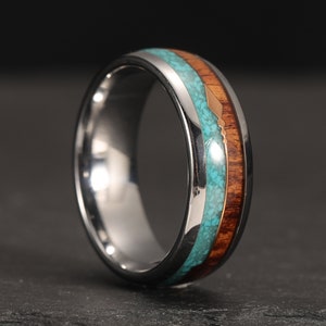 Könnte beinhalten: Ein silberner Ring mit einer Holzband und Türkis-Einlage. Das Holz ist dunkelbraun und der Türkis ist leuchtend blau. Eine dünne Goldlinie verläuft durch die Mitte des Rings.