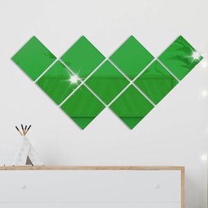 Könnte beinhalten: Ein Satz von neun grünen rautenförmigen Spiegeln, die in V-Form an einer weißen Wand angeordnet sind. Die Spiegel sind mit Klebstoff an der Wand befestigt.