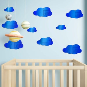 Puede incluir: Una cuna blanca con calcomanías de pared en forma de nube azul. Las nubes son reflectantes y tienen un efecto 3D.