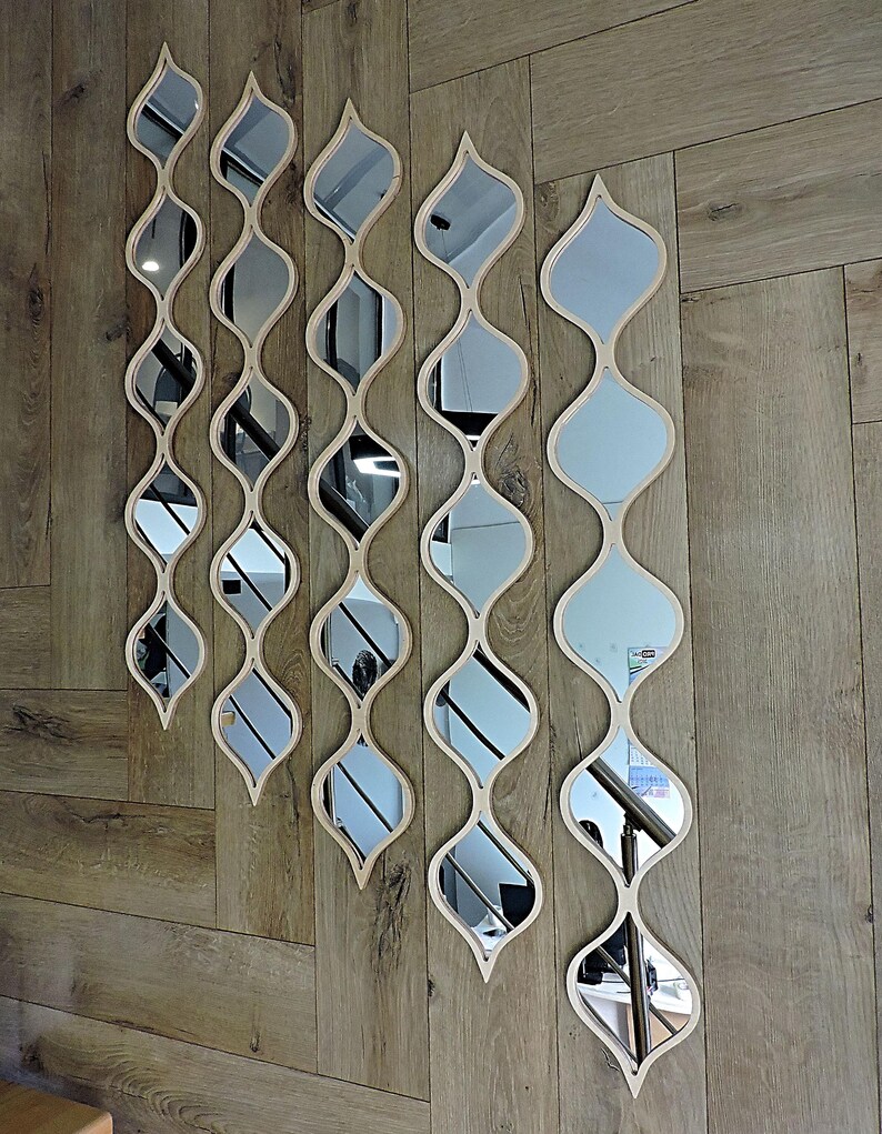 May include: A collection of decorative wall mirrors with a unique, flowing design. Each mirror features a series of interconnected, teardrop-shaped reflective surfaces, framed by light-colored wood. The mirrors are arranged vertically on a wooden wall, creating a stylish, modern aesthetic.